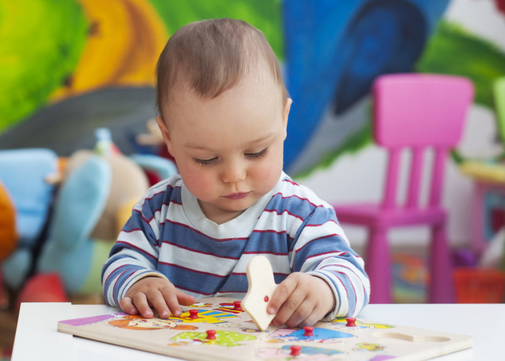 Toddler Or A Baby Child Playing With Puzzle In A Nursery 